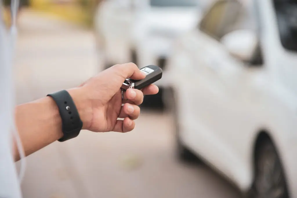 Man pressing a white car key fob with blurred vehicle in background, highlighting convenient modern auto technology