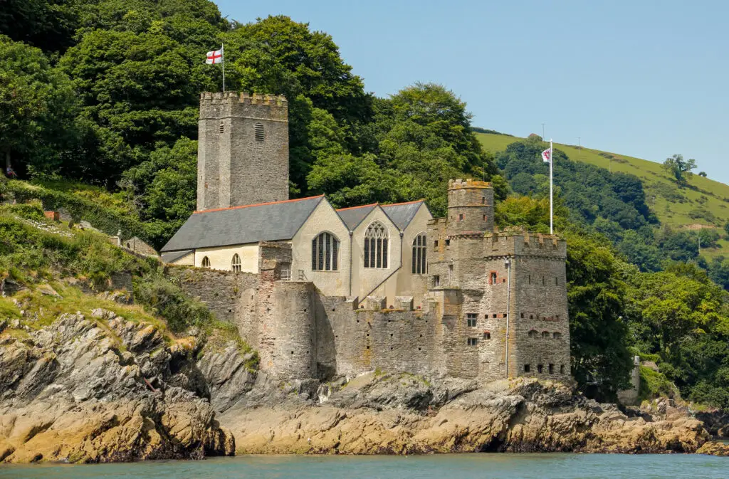 Historic Dartmouth Castle overlooking the River Dart in Devon, United Kingdom, surrounded by lush greenery and set against a clear blue sky.
