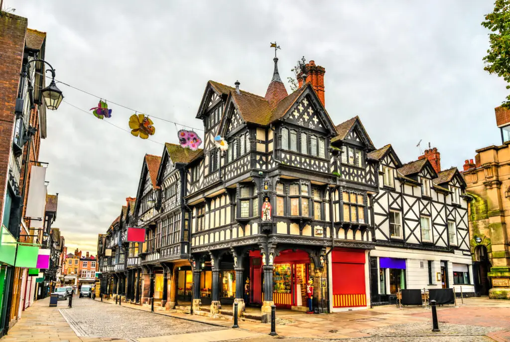 Traditional Tudor style houses in Chester, England, featuring intricate black and white timber framing, under a cloudy sky.