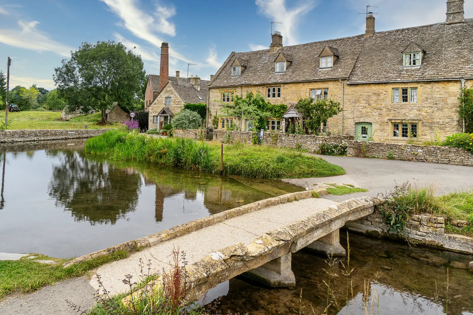 Scenic view of Lower Slaughter village in the Cotswolds, featuring charming cottages and a stone footbridge over the river, epitomizing rural England tourism.