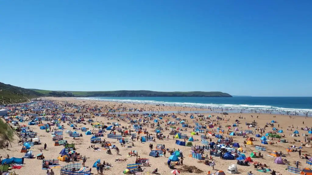 Crowded summer day at Woolacombe Beach in North Devon, showcasing a vibrant beach scene with numerous visitors enjoying the sun and sea.
