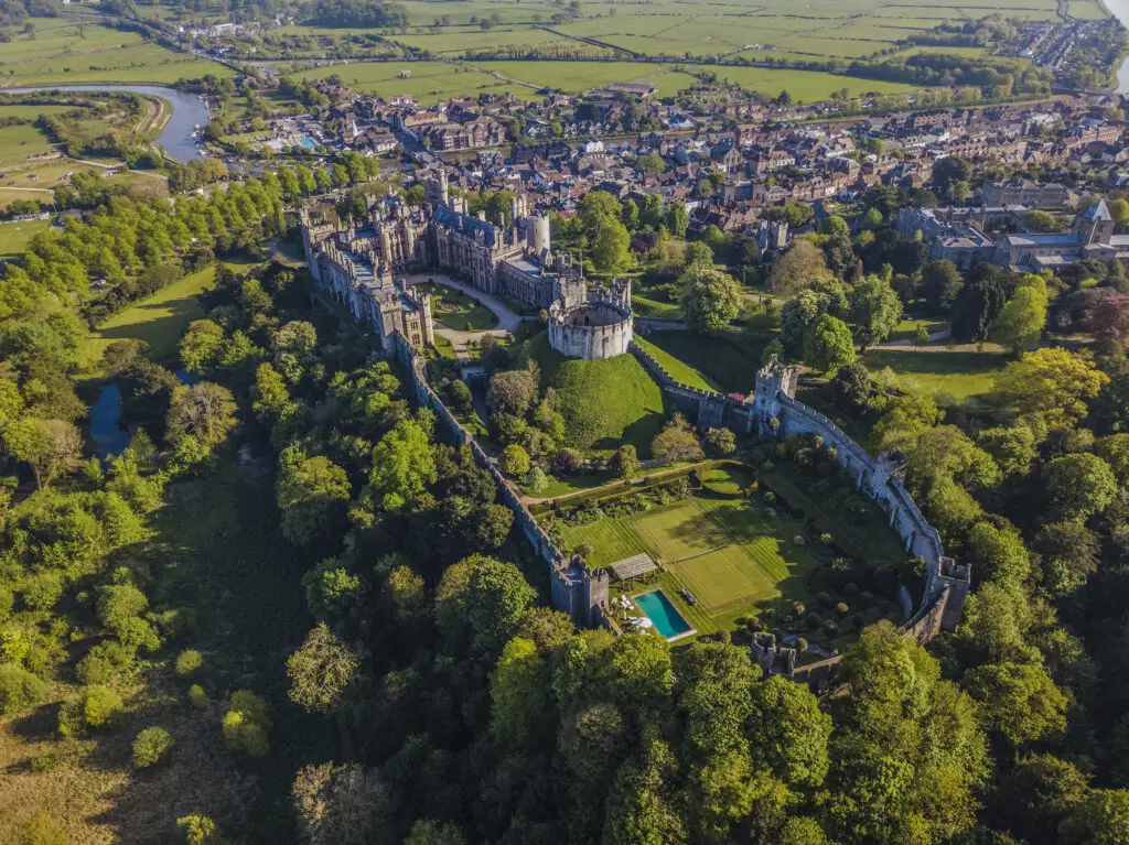 Aerial view of Arundel Castle surrounded by lush green trees and dense historical buildings, highlighting a popular tourist destination in England