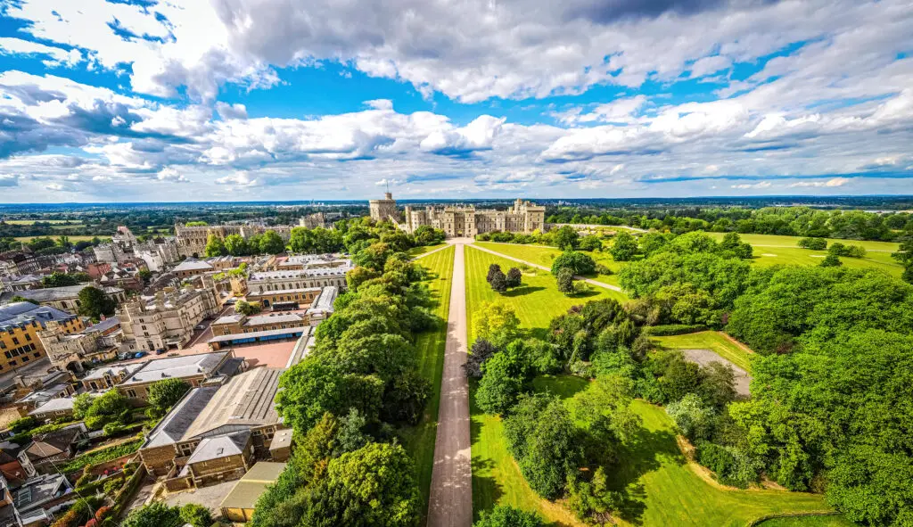Aerial view of Windsor Castle surrounded by extensive green gardens in Berkshire, England, showcasing historical architecture and lush landscapes.