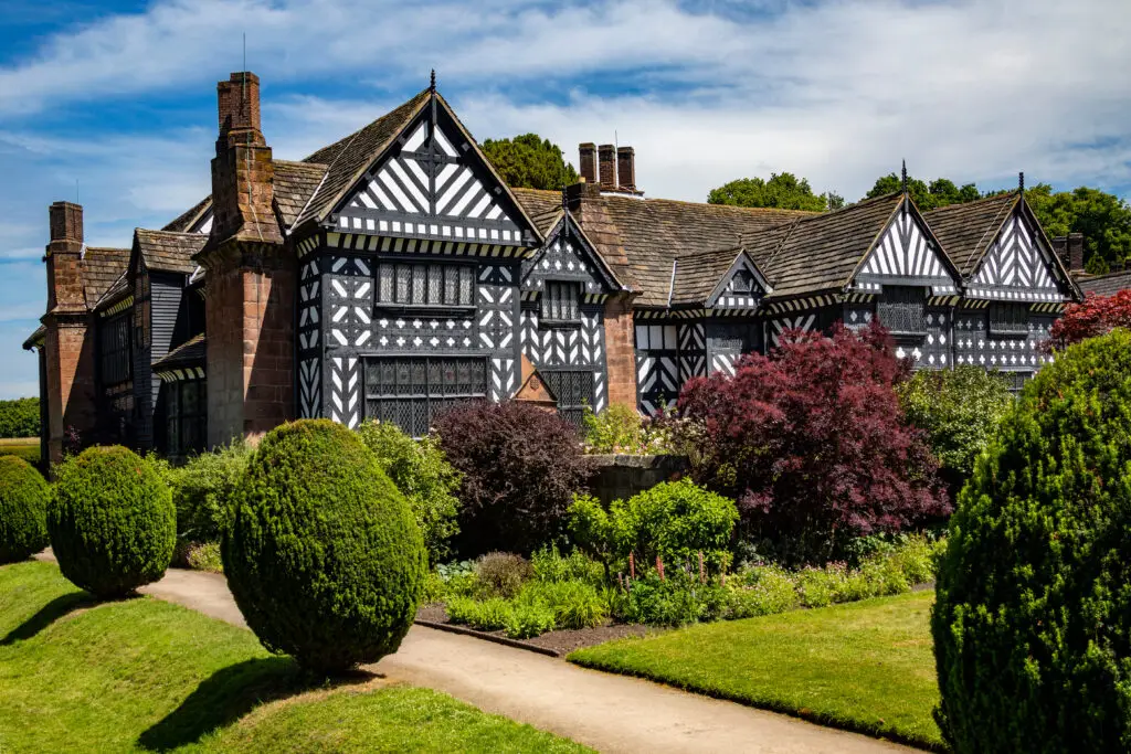Historic Speke Hall in Liverpool, United Kingdom, showcasing traditional Tudor architecture with decorative timber-framing set in a lush garden.