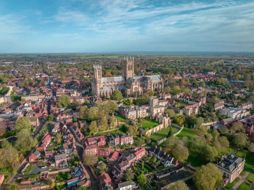 Aerial view of Lincoln Cathedral dominating the cityscape during sunset in Lincoln, England, showcasing historical architecture and lush greenery.