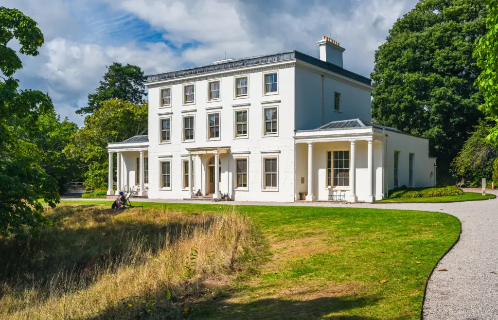 Greenway House and Garden, former home of author Agatha Christie, overlooking the River Dart in Galmpton, Devon, England, surrounded by lush greenery on a sunny day.