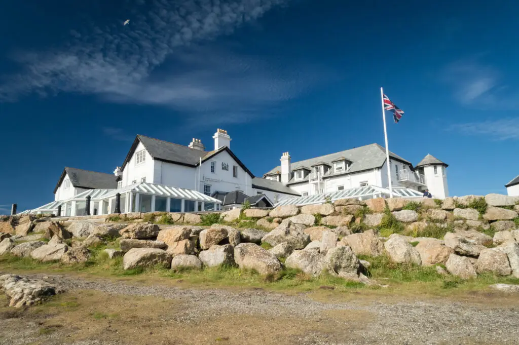 Stunning view of a white coastal hotel with a British flag flying, set against a rocky landscape and blue sky at Land's End, England.