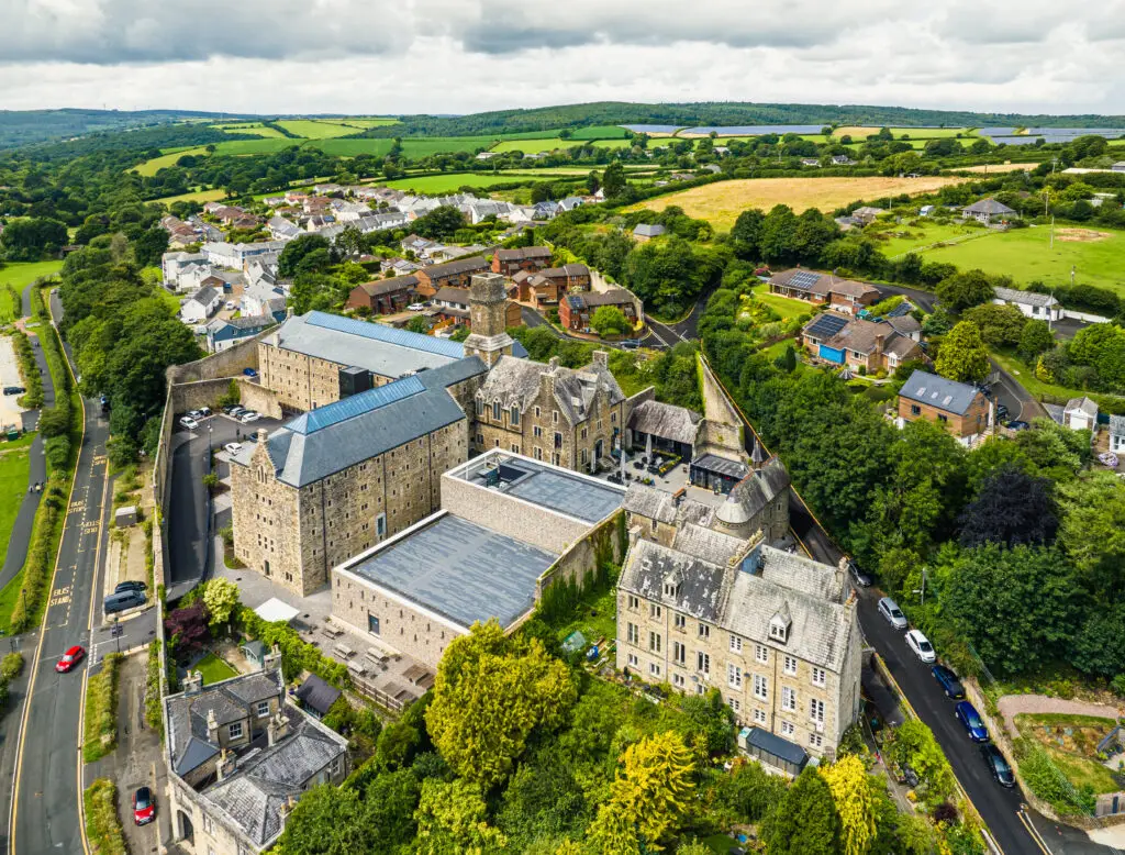 Aerial view of a historic stone building in a lush English village, showcasing the picturesque rural landscape and architecture, ideal for England Self-Drive Tours.